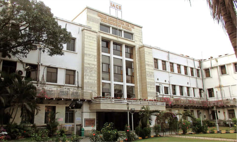 The main building of the Indian Association for the Cultivation of Science in Kolkata, a white multi-storey building behind palms and flowering shrubs.