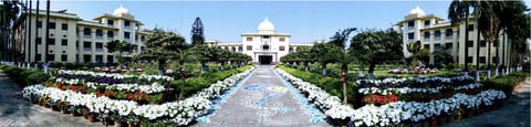 Panoramic view of Ramakrishna Mission Vidyamandira in Belur Math: a central domed building at the end of a long garden path lined with flower beds, flanked by two wings.
