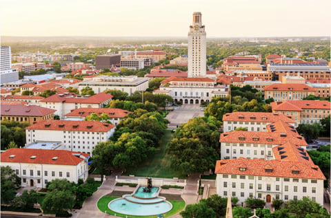 Aerial view of the University of Texas at Austin campus: the Main Building tower rising above red-tiled roofs and the Littlefield Fountain, with the city beyond.